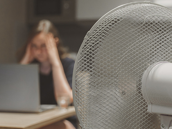 woman working at laptop in hot weather next to fan